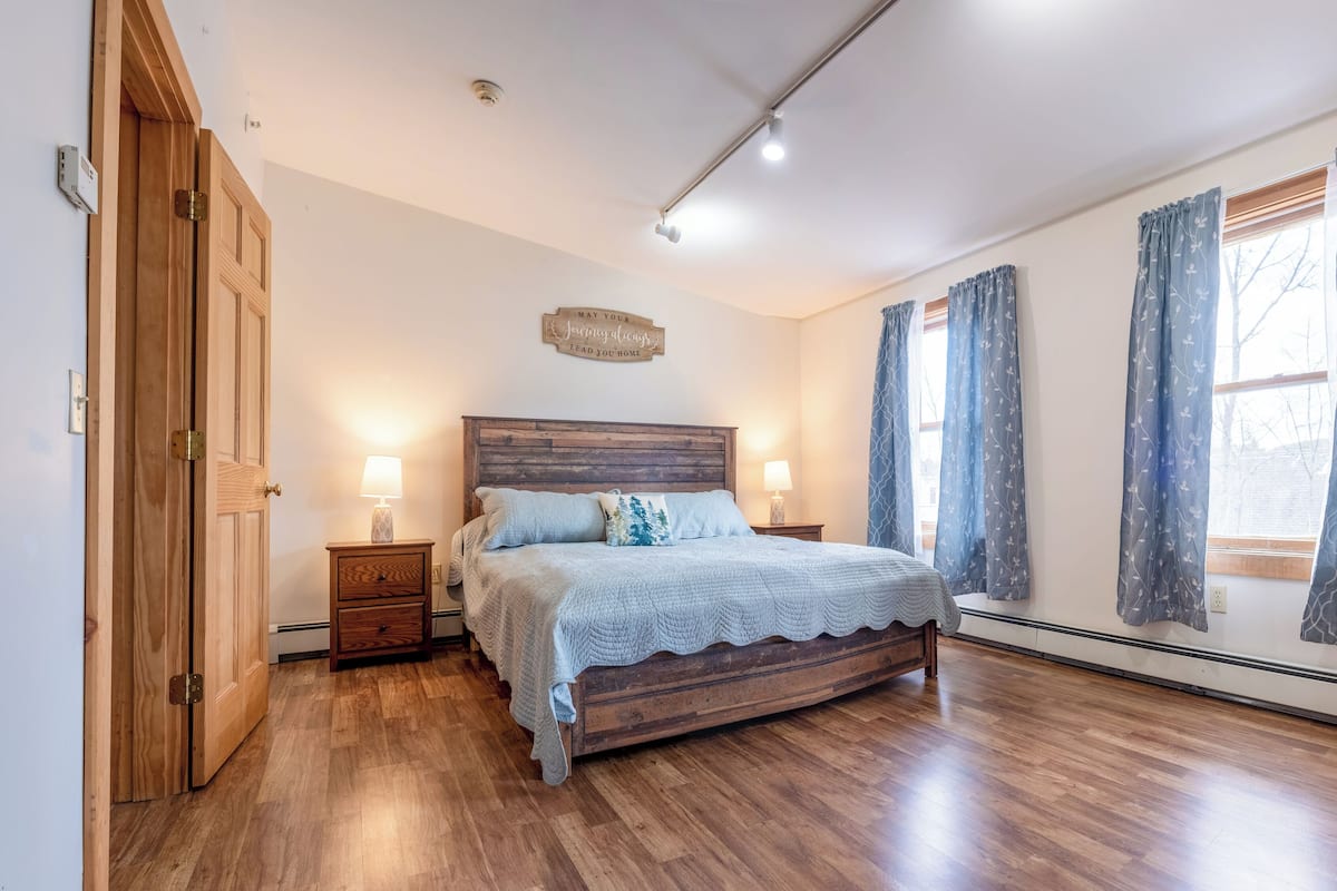 A bedroom with a wooden bed, two bedside tables with lamps, a wooden wardrobe, and a ceiling light fixture.