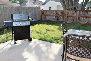 An outdoor patio with a grill, a table, and chairs.