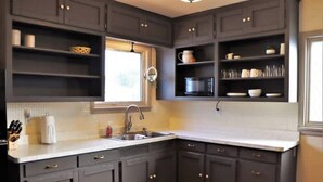 A kitchen with dark grey cabinets, a white countertop, and a window providing natural light. - Columbia House. Unique, Comfortable Cape Cod Home. Pet friendly. (Green Bay)