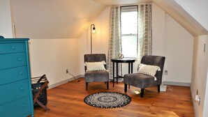 A room with a wooden floor, two armchairs, a small round table, a teal dresser, and a patterned rug. - Columbia House. Unique, Comfortable Cape Cod Home. Pet friendly. (Green Bay)