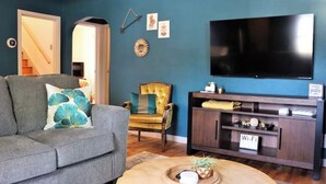 A living room with a grey sofa, a wooden armchair, a TV, and a cabinet with a 'Wi-Fi' sign. - Columbia House. Unique, Comfortable Cape Cod Home. Pet friendly. (Green Bay)