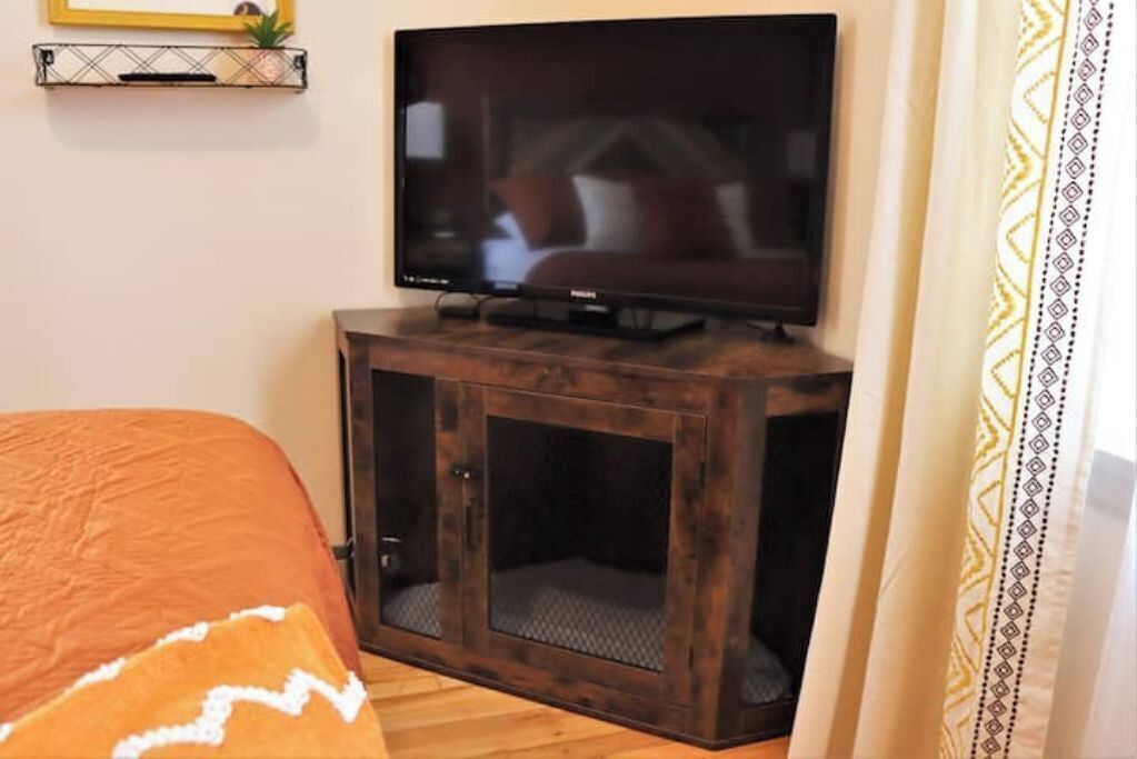 Une chambre à coucher avec un lit, un téléviseur posé sur une commode en bois et une petite étagère avec une plante.