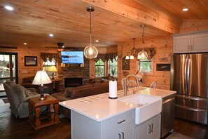 Ein gemütliches Blockhaus-Interieur mit Kamin aus Stein, Holzbalkendecke und einer modernen Küche mit Edelstahlgeräten.