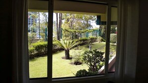 Une vue depuis une fenêtre sur un jardin bien entretenu, avec différentes plantes et un petit arbre au centre.