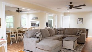 A living room with a sectional sofa, ottoman, dining area with chairs, and ceiling fans. - Alabama University Events, 5 bdrm Home by Lake, sleeps 14, 5 mil to Bryant/Denny (Northport)