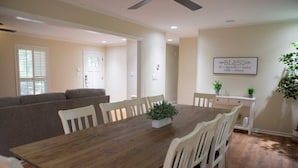 A dining area with a wooden table and white chairs, a gray sofa, and a ceiling fan. - Alabama University Events, 5 bdrm Home by Lake, sleeps 14, 5 mil to Bryant/Denny (Northport)