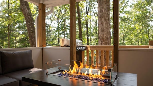 A fire feature with a glass enclosure on a wooden table in a forested outdoor area. - Alabama University Events, 5 bdrm Home by Lake, sleeps 14, 5 mil to Bryant/Denny (Northport)