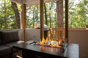 A fire feature with a glass enclosure on a wooden table in a forested outdoor area. - Alabama University Events, 5 bdrm Home by Lake, sleeps 14, 5 mil to Bryant/Denny (Northport)