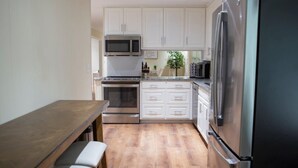 A compact kitchen with white cabinets, stainless steel appliances, and a wooden dining table. - Alabama University Events, 5 bdrm Home by Lake, sleeps 14, 5 mil to Bryant/Denny (Northport)