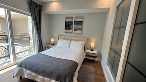 A bedroom with a bed, two bedside tables, a window with curtains, and a view of an outdoor area.