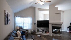 A modern living room with a leather sofa, a coffee table, a flat-screen TV, and a fireplace. - Texas Roots: King Beds - 6 Minutes to Downtown McKinney- Sleeps 6 - Remodeled (McKinney)