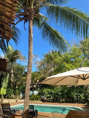 A poolside area with a palm tree, lounge chairs, and a large umbrella. - Pousada Bambu Dourado (Maraú)