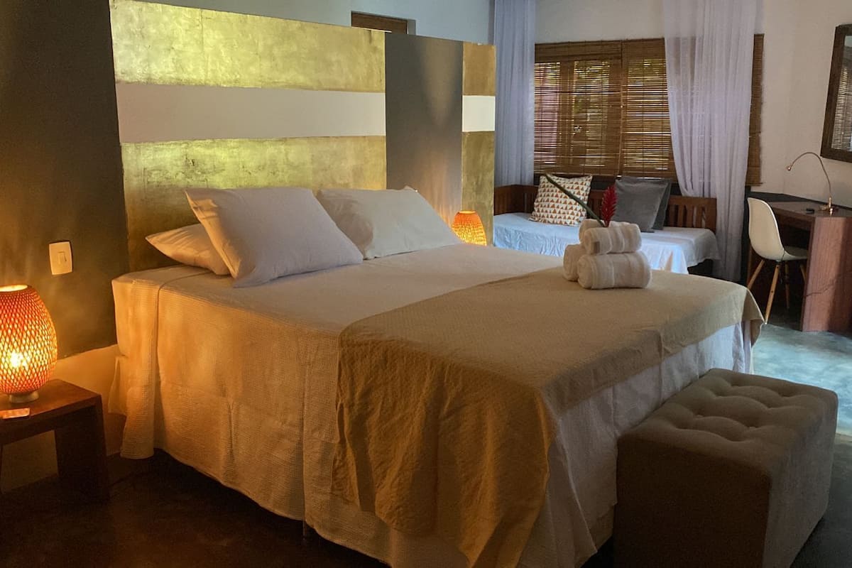 A spacious bedroom with a large bed, a bedside table with a lamp, a desk with a chair, and a window with curtains.