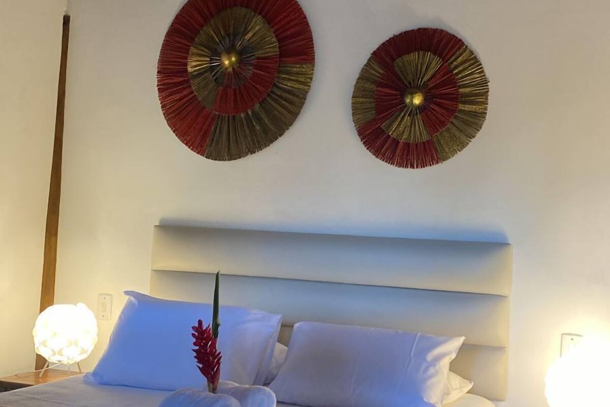 A hotel room with a wooden ceiling, two wall-mounted decorative fans, a neatly made bed with white linens, and bedside lamps.