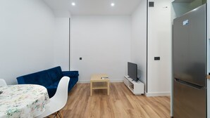 A compact living space with a sofa, a small table, a TV, and a refrigerator. - GuestReady – Enjoy Madrid in comfort and style (Madrid)