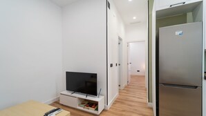 A modern apartment with a flat-screen TV on a white cabinet, a small table with a remote, and a stainless steel refrigerator. - GuestReady – Enjoy Madrid in comfort and style (Madrid)