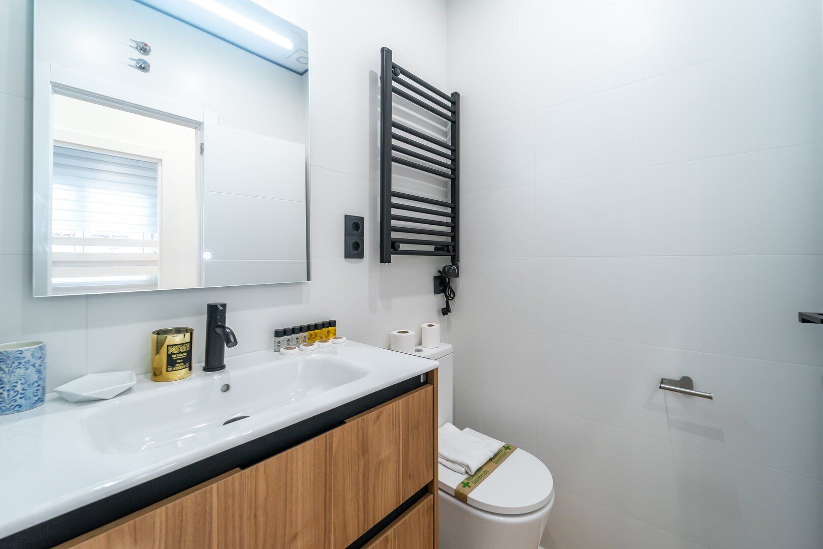Un baño moderno con un lavabo blanco, un espejo y un perchero negro.