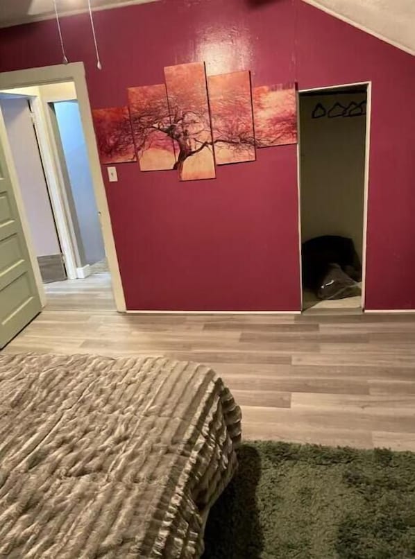 A bedroom with a bed, a painting on the wall, and a door leading to another room.
