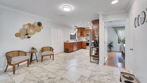 Una cocina amplia con armarios de madera, un comedor con mobiliario de mimbre y un pasillo que conduce a un invernadero.