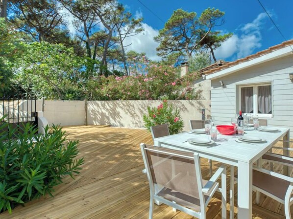 A wooden deck with a white table set for dining, surrounded by greenery and trees.