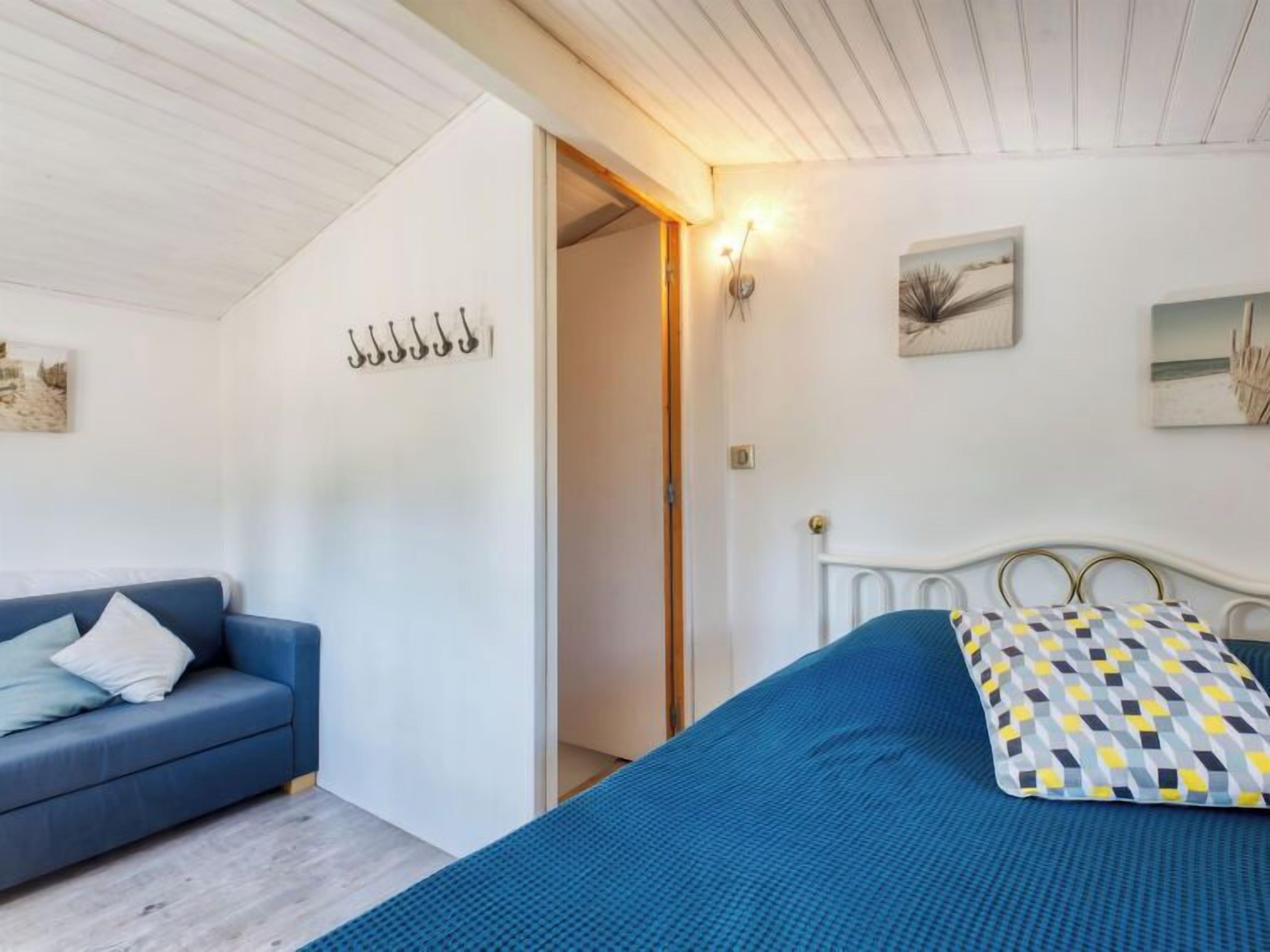 A bedroom with a bed, a blue sofa, and a door leading to another room.