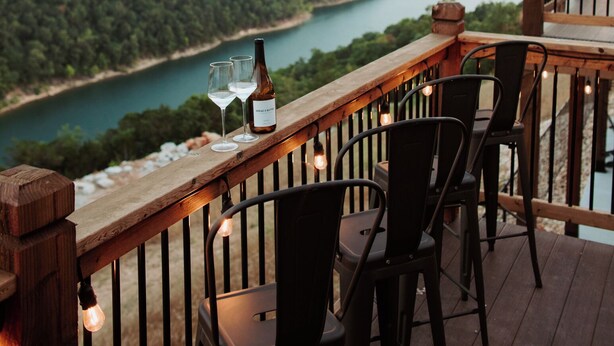 Una terraza de madera con sillas y una mesa, con vistas a un río y colinas boscosas.