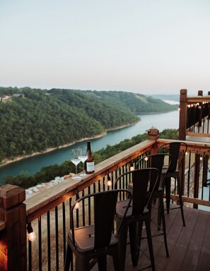 Una terraza de madera con sillas y una mesa, con vistas a un río y colinas boscosas.