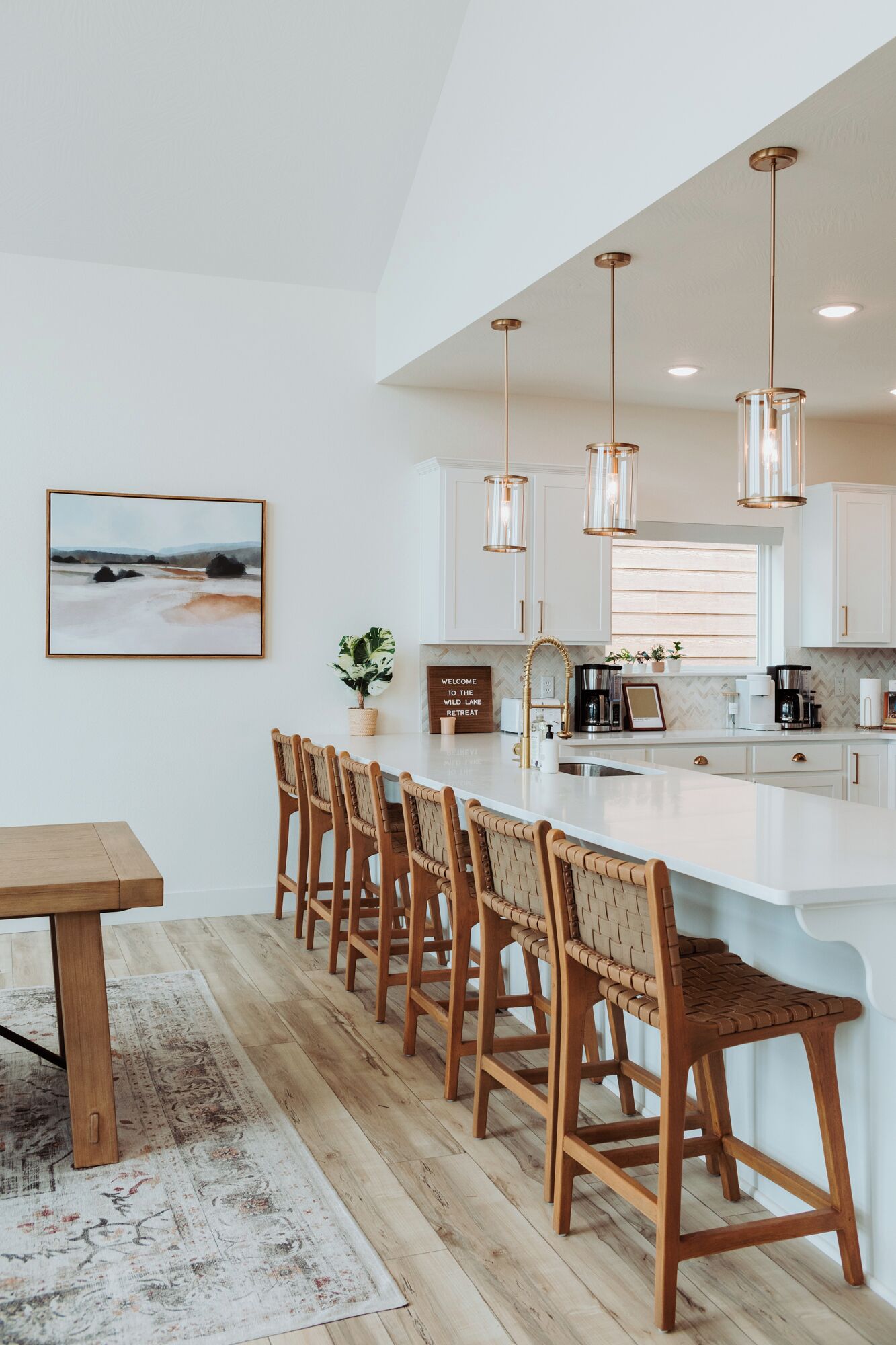 Una cocina moderna con una isla grande, luces colgantes y un conjunto de sillas de madera rústica.
