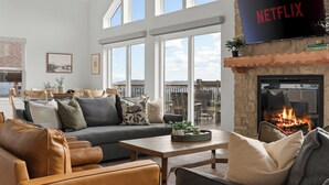 Amplia sala de estar con chimenea, un televisor grande mostrando 'NETFLIX' y un balcón con vistas.