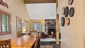 Un espace repas avec une longue table en bois et des chaises, une cheminée en pierre et des assiettes décoratives accrochées au mur.