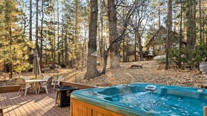 Une terrasse en bois avec un jacuzzi, du mobilier d’extérieur et un paysage boisé en arrière-plan.