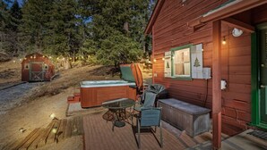 Een houten hut met een hottub, terras en een kleine schuur, gelegen in een bosrijk gebied.