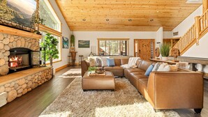 A spacious living room with a stone fireplace, a large sectional sofa, and a wooden ceiling. - Stunning, like-new, 4-bedroom log-style cabin home. (Big Bear Lake)
