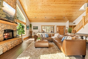 A spacious living room with a stone fireplace, a large sectional sofa, and a wooden ceiling.