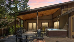 A covered outdoor patio with a fire pit, seating, and a hot tub. - Stunning, like-new, 4-bedroom log-style cabin home. (Big Bear Lake)