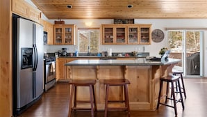 Una cocina con armarios de madera, un refrigerador de acero inoxidable, una isla grande con taburetes y vistas al exterior.