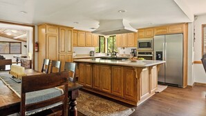A kitchen with wooden cabinets, a stainless steel refrigerator, a microwave, and a dining area with a table and chairs. - Double Black Diamond | Bear Mtn w/ Hot Tub (Big Bear Lake)