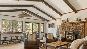 A cozy living room with a stone fireplace, leather sofas, and a large window overlooking a deck. - Double Black Diamond | Bear Mtn w/ Hot Tub (Big Bear Lake)