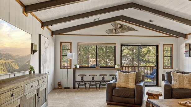 A spacious living room with a large window, a wooden cabinet, and a leather sofa. - Double Black Diamond | Bear Mtn w/ Hot Tub (Big Bear Lake)
