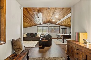 A loft-style living room with a high ceiling, wooden beams, a fireplace, a pool table, and a cozy seating area.