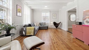 Ein geräumiges Wohnzimmer mit Holzboden, einem grauen Sofa, einem weißen Sessel und einer rosa Kommode.