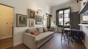 A living room with a sofa, dining table, and chairs, a chandelier, and framed pictures on the wall. - Ognissanti Flat in Florence by Mmega (Firenze)