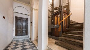 A hallway with a checkered floor, a wooden door, and a staircase with a metal railing. - Ognissanti Flat in Florence by Mmega (Firenze)
