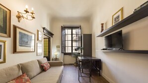 A compact living space with a sofa, a dining table, a TV, and artwork on the walls. - Ognissanti Flat in Florence by Mmega (Firenze)