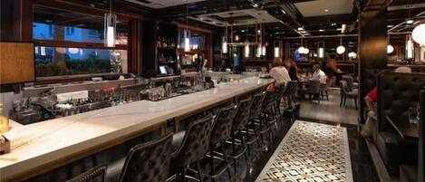A bar area with a long counter, multiple bar stools, and a patterned rug.