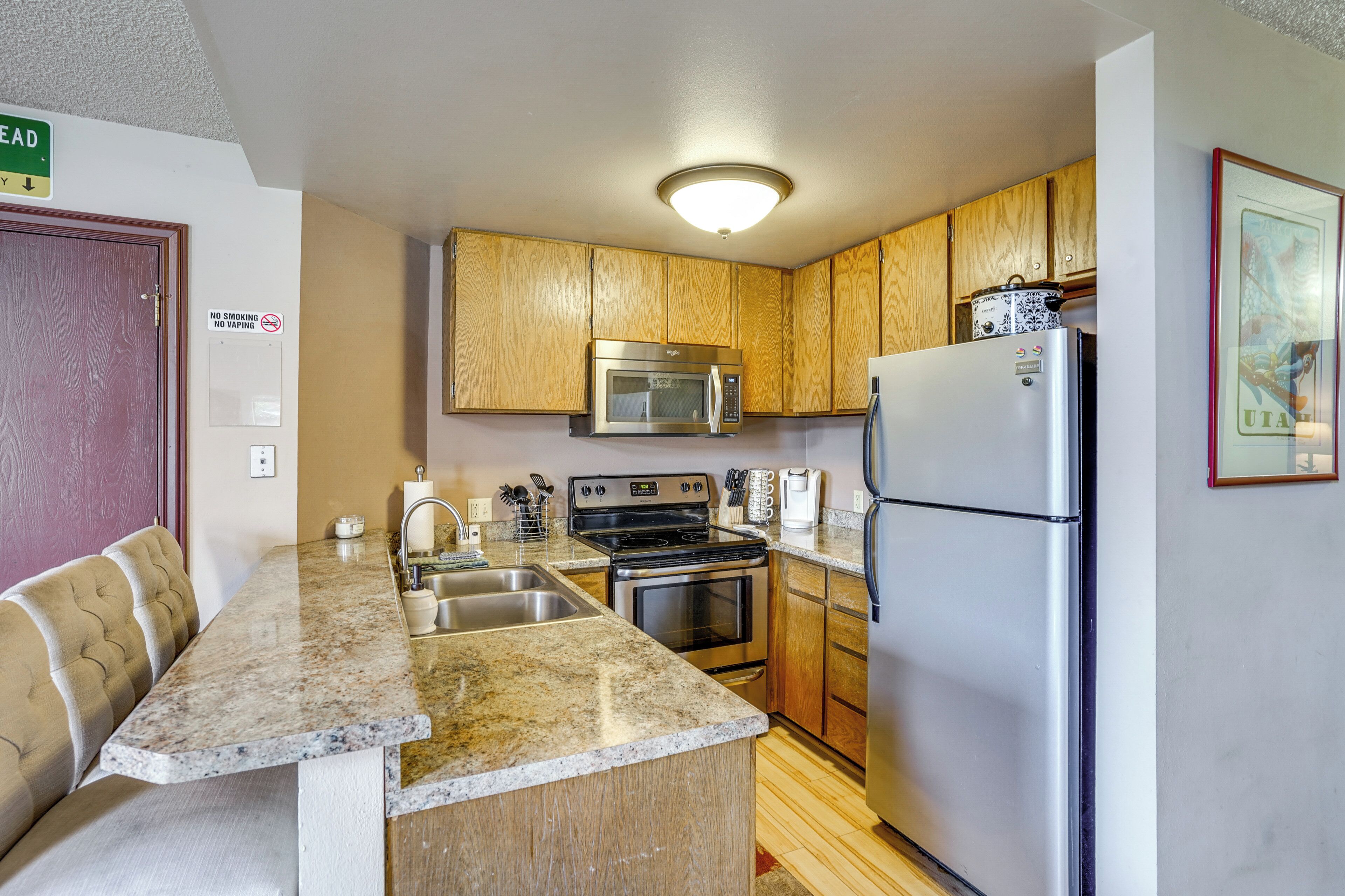 A compact kitchen with wooden cabinets, a stainless steel refrigerator, a microwave, and a stove.
