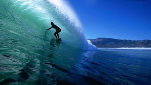 Un surfista cabalgando una ola grande, con vista despejada al océano y accidentes geográficos lejanos.