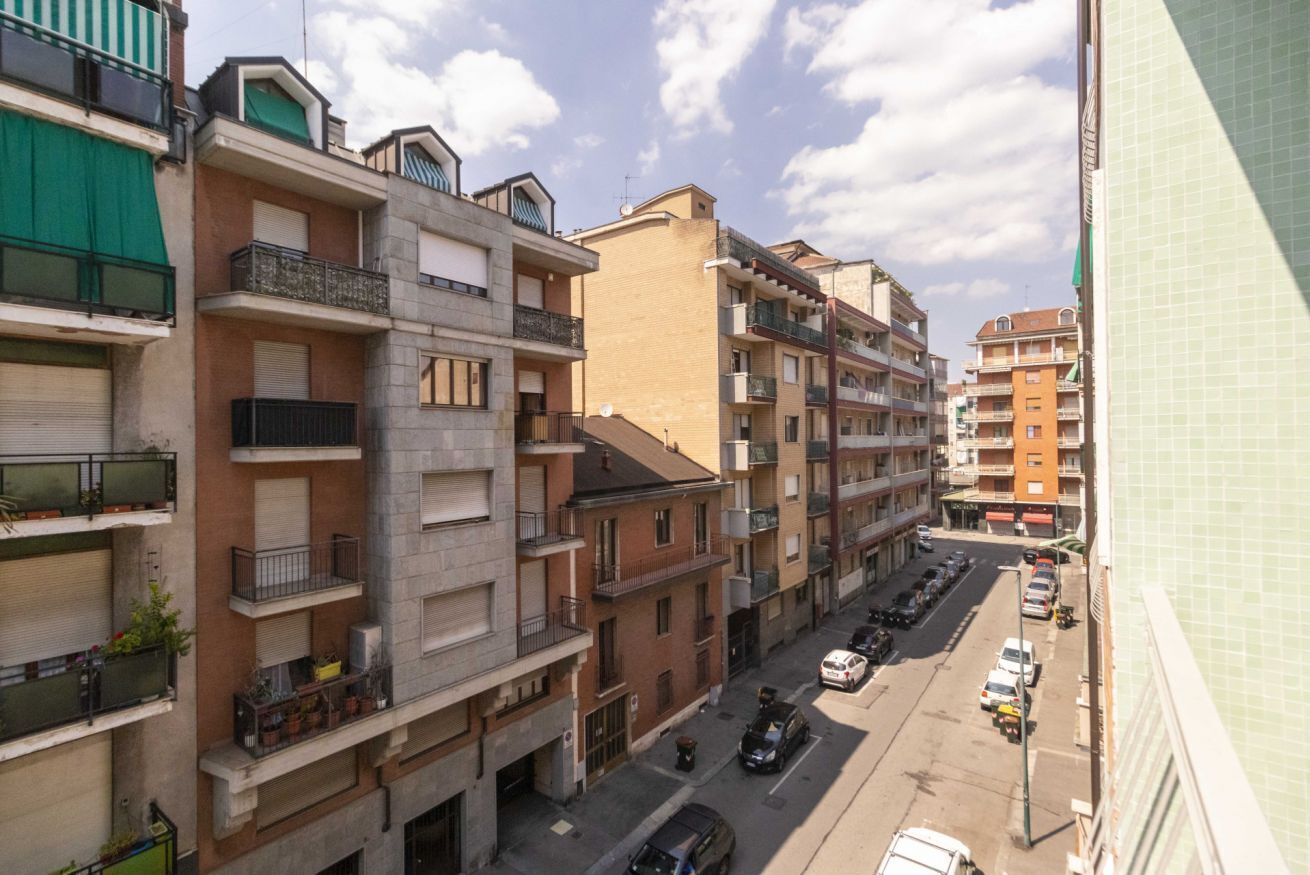 A multi-story residential building with balconies, a street in front, and parked cars.