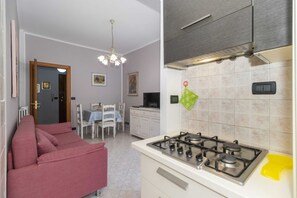 A compact kitchen with a gas stove, a dining area with a table and chairs, and a sofa. - GuestHost - Santa Rita Neighborhood! Comfortable Appt x3 (Torino)