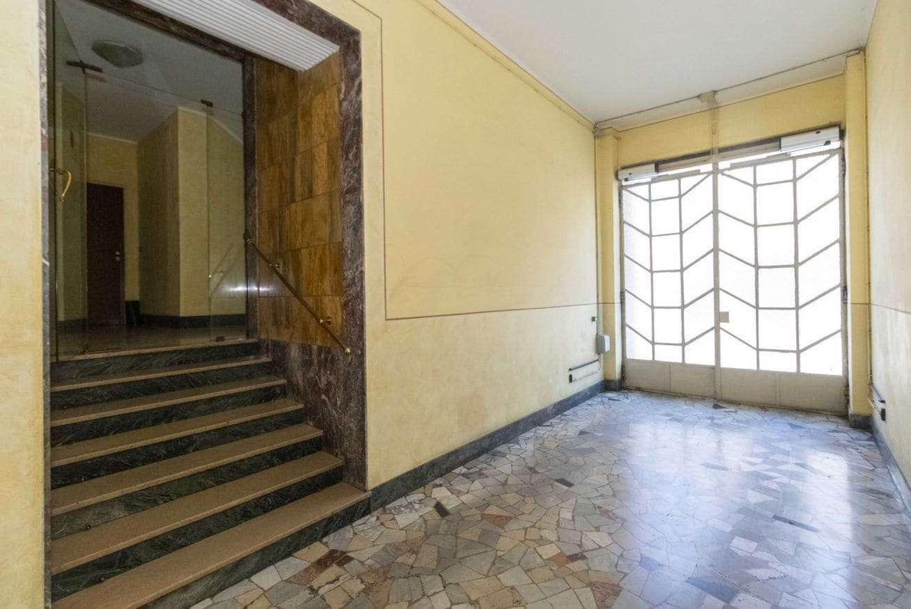 A hallway with a marble staircase, a patterned floor, and a large window with a geometric design.